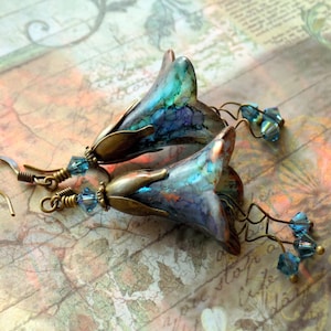 May include: A pair of blue and purple flower-shaped earrings with crystal accents. The earrings are made of metal and glass.