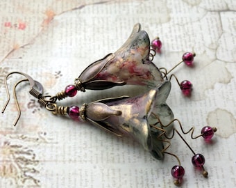 May include: A pair of floral earrings with a bell-shaped design. The earrings are made of metal and have a vintage look. They are decorated with pink, white, and green paint and have a gold finish. The earrings are accented with small, dark red beads.