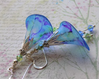Pode incluir: Um par de brincos de aquarela azul e roxo com detalhes prateados e gotas de cristal.