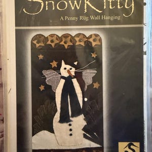 May include: A craft pattern package titled Folk Art SnowKitty A Penny Rug Wall Hanging by Crane Design. The cover features a white cat figure with a dark blue scarf, wings, and a carrot nose, set against a dark background with gold stars.