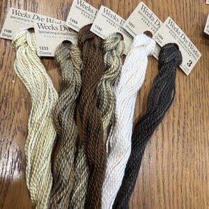 May include: Five skeins of Weeks Dye Works Pearl Cotton embroidery thread in various neutral shades. The colors include 1106 Beige, 1233 Cocoa, 1269 Chestnut, 1198 London Fog, 1091 Whitewash, and 1304 Onyx, each with a branded paper tag attached.