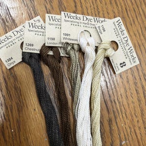 May include: Five skeins of Weeks Dye Works Pearl Cotton 8 embroidery thread in colors Onyx, Chestnut, London Fog, Whitewash, and Beige. Each skein is attached to a branded paper tag labeled with the color name, number, and 10 yards length.