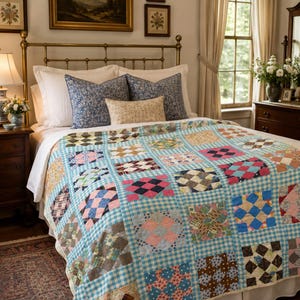 May include: A patchwork quilt featuring a grid of squares with various floral, plaid, and geometric patterns in shades of pink, blue, brown, and white, separated by a light blue and white gingham border, draped over a bed with white pillows.