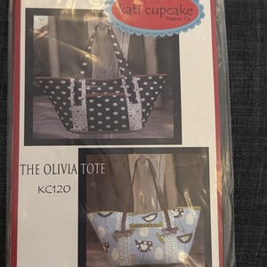 May include: A sewing pattern packet titled The Olivia Tote KC120 by Kati Cupcake Pattern Co. The packaging features two photographs of tote bags: one black with white polka dots and another light blue with a bird and egg pattern and brown straps.