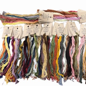 May include: A collection of embroidery floss skeins in a wide variety of colors, each attached to a tan paper tag labeled Simply Shaker The Gentle Art. The threads are arranged in rows, displaying shades of blue, green, yellow, red, and pink.