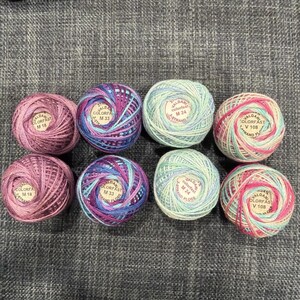 May include: Eight round balls of Valdani colorfast embroidery floss arranged in two rows. The colors include variegated shades of pink, purple, blue, and light green. Each ball features a central label with text including M18, M33, M24, and V108.