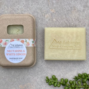 May include: A bar of handmade soap in a cardboard box with a peach and white floral design. The soap is labeled "Nectarine & White Ginger" and "Mt Lebanon Soap Company, LLC".