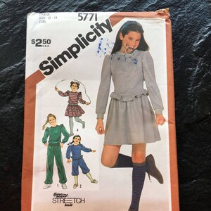 Może przedstawiać: Wzór szycia Simplicity numer 5771 dla dziewczynek w rozmiarach 12-14. Wzór zawiera cztery różne style odzieży: sukienkę z długimi rękawami i falbanką na dole, bluzkę z długimi rękawami i falbanką na dole, bluzkę z długimi rękawami i falbanką na dole oraz spodnie, a także bluzkę z długimi rękawami i falbanką na dole oraz spodenki. Wzór jest przeznaczony do dzianin i zawiera instrukcje dotyczące wyboru odpowiedniej dzianiny do projektu.