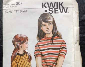 Könnte beinhalten: Ein Vintage-Schnittmuster für ein Mädchen-T-Shirt. Das Schnittmuster ist von Kwik Sew und ist für die Größen 8-10-12. Das Schnittmuster zeigt zwei Mädchen, die das Shirt tragen, eines mit einem gestreiften Muster und das andere mit einem karierten Muster.