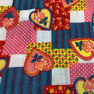 May include: A patchwork fabric with a repeating pattern of hearts featuring roses and leaves. The fabric is in shades of red, pink, yellow, and blue.