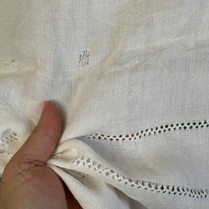 May include: White fabric with a delicate lace trim. The fabric is slightly creased and has a few small holes.