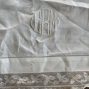 May include: White linen tablecloth with a delicate lace trim and embroidered initials "ERM" in the center.