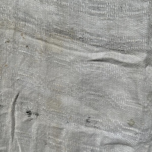 May include: A white linen fabric with a woven texture. The fabric has a few small brown stains.