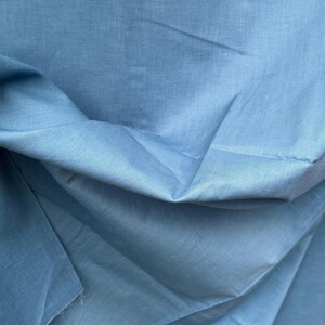 May include: A close-up of a light blue fabric with a smooth texture. The fabric is folded and draped, showing its soft and flowing nature.