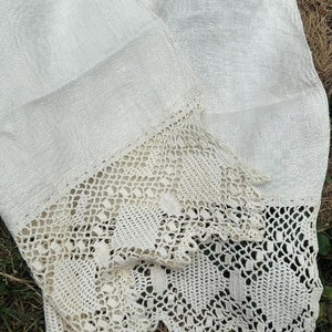 May include: A white linen tablecloth with a crocheted lace border. The tablecloth is folded in half and has a subtle herringbone pattern.