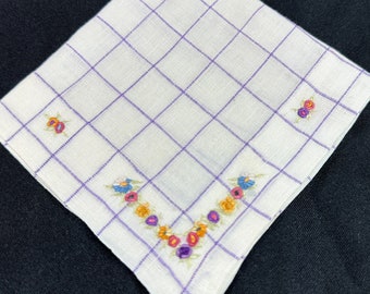 May include: A white handkerchief with a purple grid pattern and a floral design embroidered around the edges. The flowers are in shades of pink, yellow, and blue.