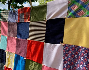 May include: A patchwork quilt made of various fabrics in different colors and patterns, including red, blue, green, yellow, and pink. The quilt is hanging on a clothesline outdoors.