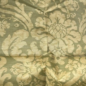 May include: Close-up of a fabric with a repeating damask pattern. The design features large, stylized floral and leaf motifs in a light beige colour against a muted green background. The fabric has a subtle sheen.