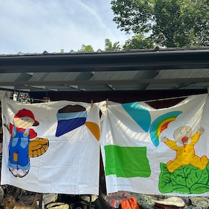 May include: Two colorful fabric panels with cartoon characters. The first panel features a red-haired boy wearing a blue shirt and overalls holding a baseball bat. The second panel features a baby wearing a yellow shirt and a blue pacifier, sitting on a green cloud with a white border.