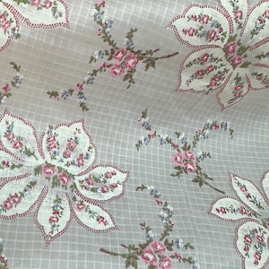 Puede incluir: Tela floral con un fondo de patrón de cuadrícula. Grandes formas de flores blancas con acentos rosas y rojos están dispersas por la tela. También hay ramitas florales rosas y azules más pequeñas, creando un diseño delicado y femenino.