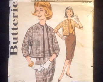Può includere: Busta di cartamodello vintage con un set di gonna e giacca a quadri marroni e bianchi. Il cartamodello è di Butterick ed è per la taglia 10. La busta include anche il testo "One Yard Line" e "Quick 'N Easy".