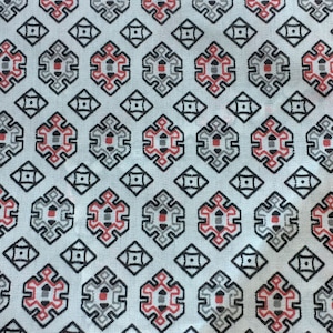 May include: Close-up of a white fabric with a repeating geometric pattern. The pattern features black, red, and gray shapes arranged in a grid-like design. The fabric appears to be folded, showing the pattern's continuity.