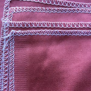 May include: Close-up of a burgundy fabric with three rows of white stitching along the edge.