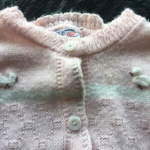 Può includere: Cardigan rosa chiaro con motivo a maglia strutturata e chiusura con bottoni. Il maglione presenta piccole applicazioni di animali bianchi e soffici, tra cui un topo e un'anatra. Il colletto e l'abbottonatura sono a coste.