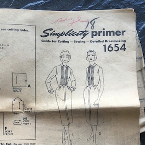 May include: A vintage Simplicity sewing pattern guide for dressmaking, featuring a black and white illustration of a woman wearing a dress with a skirt and a bodice. The pattern number is 1654 and the size is 18. The guide includes instructions for cutting, sewing, and detailed dressmaking.