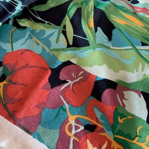 K&ouml;nnte beinhalten: Ein schwarzer Stoff mit einem farbenfrohen Blumenmuster. Der Stoff zeigt gro&szlig;e rote Blumen mit gr&uuml;nen Bl&auml;ttern und einem blauen Hintergrund. Der Stoff ist strukturiert und hat ein weiches Gef&uuml;hl.
