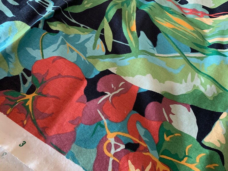 K&ouml;nnte beinhalten: Ein schwarzer Stoff mit einem farbenfrohen Blumenmuster. Der Stoff zeigt gro&szlig;e rote Blumen mit gr&uuml;nen Bl&auml;ttern und einem blauen Hintergrund. Der Stoff ist strukturiert und hat ein weiches Gef&uuml;hl.