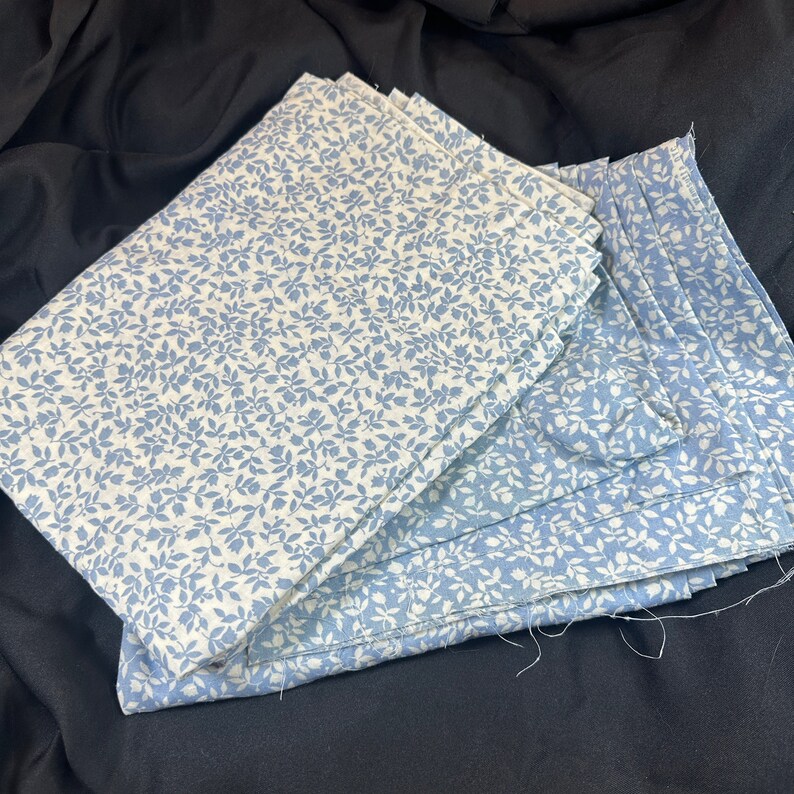 May include: A stack of blue and white fabric with a floral pattern. The fabric is folded and has a light blue background with white floral designs.