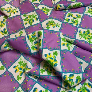 Pu&ograve; includere: Tessuto viola con un motivo a trifoglio bianco e verde. Il tessuto &egrave; piegato e presenta un motivo a rombi.
