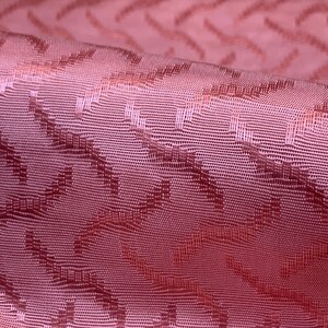 May include: Close-up of a pink fabric with a textured, geometric pattern. The fabric has a subtle sheen and a soft, drapey feel.
