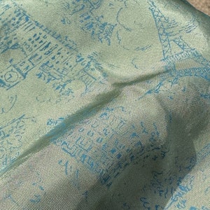 May include: A close-up of a green fabric with a blue pattern. The fabric has a woven texture and is slightly wrinkled.