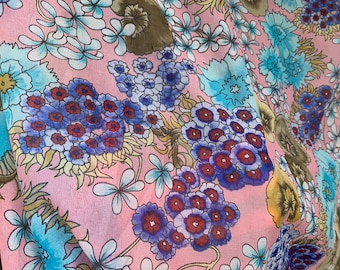 May include: Pink fabric with a floral pattern featuring blue, red, and yellow flowers. The fabric has a soft, flowing texture.