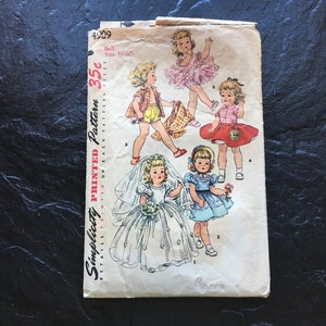 Puede incluir: Patrón de costura vintage Simplicity para ropa de muñeca. El patrón es para una muñeca de 40,6 cm e incluye cinco atuendos diferentes: un vestido de novia blanco, un vestido azul, una falda roja con una blusa blanca, una falda rosa con una blusa blanca y una falda a cuadros con una blusa blanca. El patrón está impreso en papel blanco con un borde rojo y negro.