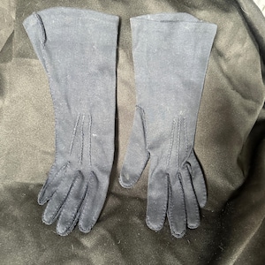 Puede incluir: Un par de guantes largos negros hechos de una tela suave. Los guantes tienen un diseño sencillo con una costura en la parte posterior de cada guante.