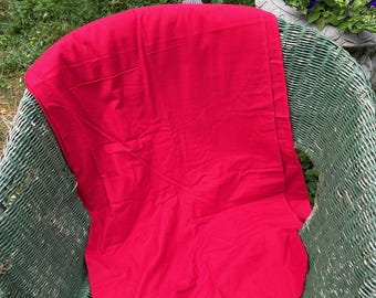 Peut inclure: Un tissu rouge vif drapé sur une chaise en osier. Le tissu est lisse et semble être en coton.