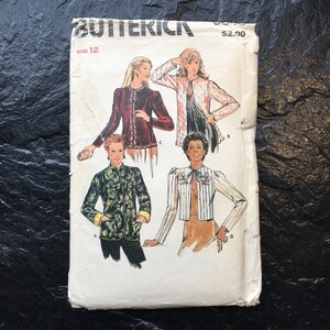 Puede incluir: Patrón de costura vintage para una blusa de mujer. El patrón es de Butterick y es de talla 12. El patrón muestra tres estilos diferentes de blusas, una con estampado floral, otra con estampado a rayas y otra con un color sólido.