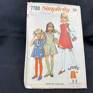 以下が含まれることがあります： 女の子のドレス用のシンシティ・ソーイングパターン番号7783。パターンは、バストが27インチのサイズ8用です。パターンカバーには、異なるスタイルのドレスを着た3人の女の子が描かれています。パターンカバーには「ジフィー」という文字が印刷されています。