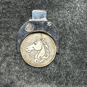 May include: A silver-toned metal token with a horse head design. The token is attached to a silver-toned metal clip.