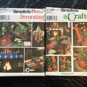 Könnte beinhalten: Zwei Simplicity-Nähmuster für Weihnachtsbastelarbeiten. Das Muster auf der linken Seite ist für die Dekoration des Hauses und beinhaltet einen Baumrock, eine Kaminsimsdekoration und einen Tischläufer. Das Muster auf der rechten Seite ist für Bastelarbeiten und beinhaltet einen Strumpf, einen Baumrock und Ornamente. Beide Muster sind in Einheitsgröße.
