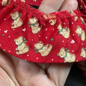 Könnte beinhalten: Roter Stoffbesatz mit weißem Tupfenmuster und einem sich wiederholenden Muster aus braunen Teddybären mit grünen Schleifen.