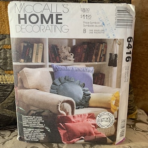 Può includere: Modello di decorazione per la casa McCall's numero 6416 per cuscini. Il modello include istruzioni per realizzare cuscini in varie forme e dimensioni, tra cui stili arricciati, su misura e arricciati. La copertina del modello presenta una foto di un soggiorno con una poltrona e diversi cuscini.