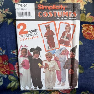 Könnte beinhalten: Ein Simplicity 7984 Schnittmusterumschlag für Kinderkostüme, Größe A (1-4). Das Cover zeigt Illustrationen verschiedener Outfits, darunter ein Teufel, eine Maus, ein Engel, ein Narr und eine Hexe, aus der 2 Hour Express Collection.