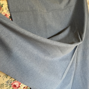 May include: A close-up of a blue fabric with a subtle texture. The fabric is folded and draped over a floral patterned surface.