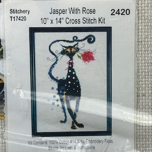 May include: A cross-stitch kit titled "Jasper With Rose" featuring a whimsical black cat holding a red rose. The kit includes embroidery floss, beads, needles, and instructions. The finished design measures 10 inches by 14 inches.