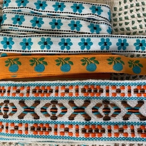 May include: Four different types of colourful woven ribbon trim. The ribbons feature geometric patterns in orange, brown, blue and white.
