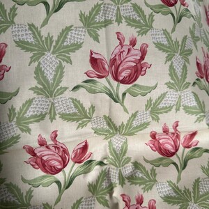 May include: Cream-colored fabric with a repeating pattern of pink tulips and green leaves. The design also includes stylized pineapple shapes in white and green, creating a floral and tropical theme.
